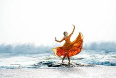 a woman in an orange dress is dancing on the beach