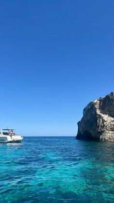 a boat is in the water next to a large rock outcropping and blue sky