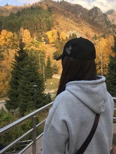 a woman standing on top of a metal railing next to a forest filled with trees