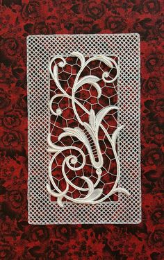 an intricately designed piece of paper on red fabric with white lace and flowers in the center