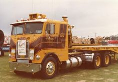 a large yellow truck parked on top of a grass covered field next to other trucks
