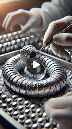 two hands in white gloves are working on an object with silver paint and metal beads