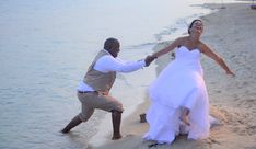 a bride and groom holding hands on the beach