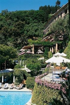 an outdoor swimming pool surrounded by trees and lawn chairs with umbrellas on the side