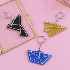 three keychains with different shapes and colors on pink surface next to each other