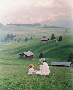 a woman and child sitting in the grass on top of a hill looking at each other