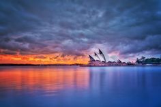 the sydney opera house is lit up at sunset with clouds in the sky above it