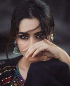 a close up of a person wearing jewelry and holding her hand near her face with both hands