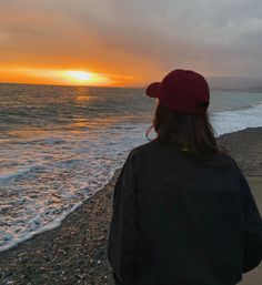 a person standing on the beach watching the sun go down over the ocean with waves coming in