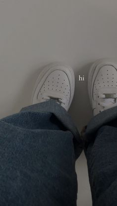 the bottom view of someone's feet wearing white tennis shoes and blue jeans with an h on them