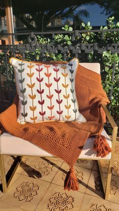 an orange and white pillow sitting on top of a wooden chair next to a plant