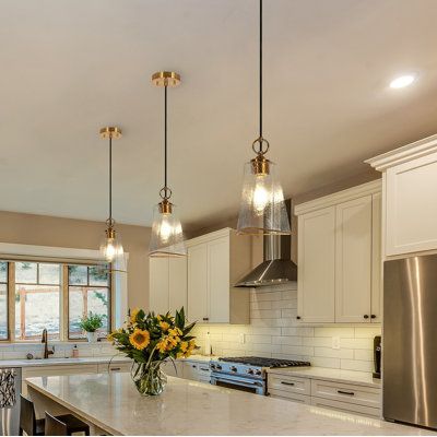 Doubling as a lighting source and fashioned decorative piece, this single pendant lighting fuses elegance and luxury. With a sleek design, the cylinder frame features a hammered glass embedded visual-delight texture, exuding an air of sophistication and luxury. The brim of the glass is painted with stain gold and the hardware is electroplated in an elegant brass finish that pairs well with the textured clear glass that strikes a harmonious balance of colors and textures. The lighting from one Ty Small Pendant Lights Over Kitchen Island, Brass Pendant Lights Over Kitchen Island, Kitchen Pendant Lights Over Island, Yellow Kitchen Paint, Mercury Glass Pendant Light, Light Yellow Paint, Black Pendant Light Kitchen, Modern Island Lighting, Gold Kitchen Hardware