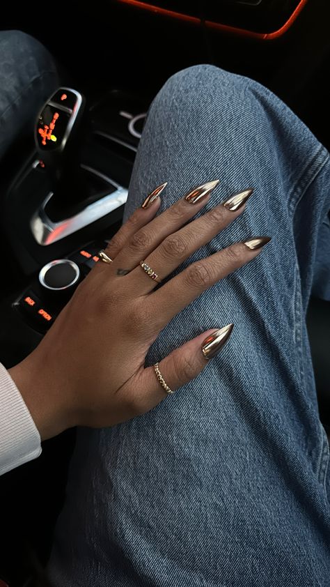 Gold chrome gel-x medium stiletto nails on a black girl’s hand while wearing gold jewelry and rings Chrome Nails Dark Skin, Chrome Nails Dark, Nails Dark Skin, Black Chrome Nails, Gold Chrome Nails, Crome Nails, Bronze Nails, Gold Acrylic Nails, Nails Dark