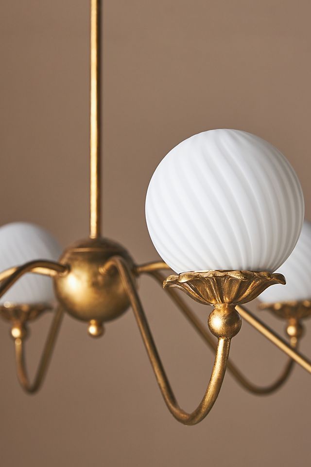 a chandelier with three white glass balls hanging from it's arms and two gold chains