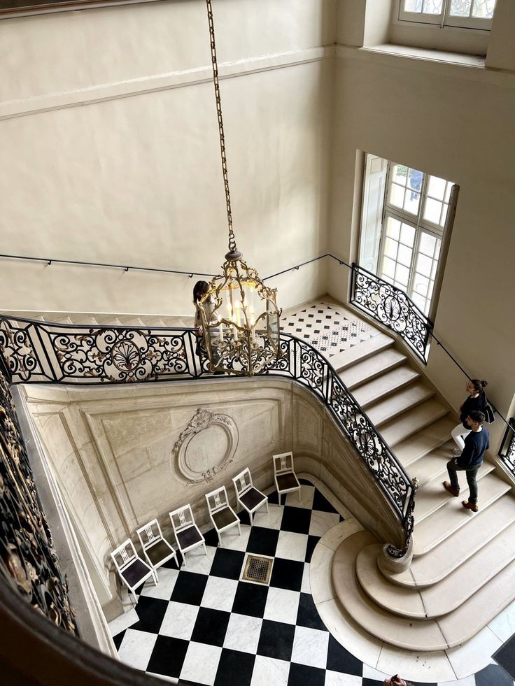 a chandelier hanging from the side of a staircase next to a black and white checkered floor