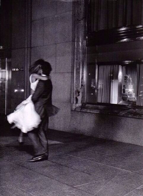 a man and woman walking down the sidewalk in front of a building at night time