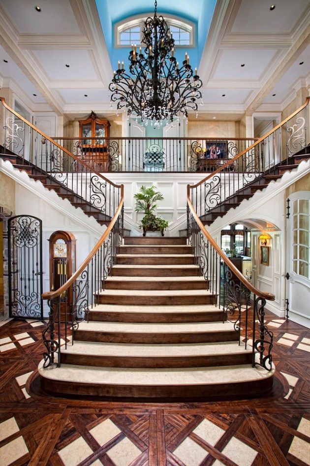 an elegant staircase with wrought iron railings and chandelier in a large home