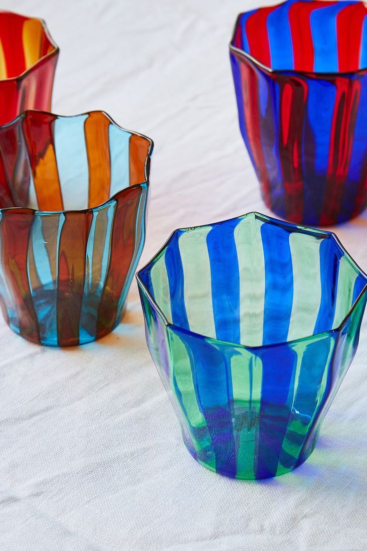 three colorful glass bowls sitting on top of a white cloth covered table next to each other