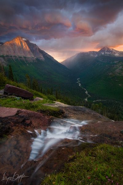 the mountains are covered in green grass and water as the sun is setting over them