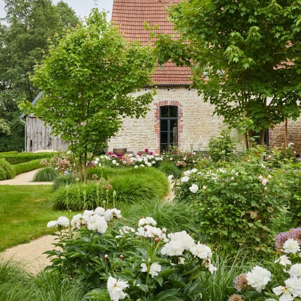 the garden is full of flowers and plants in front of an old brick building with a red roof