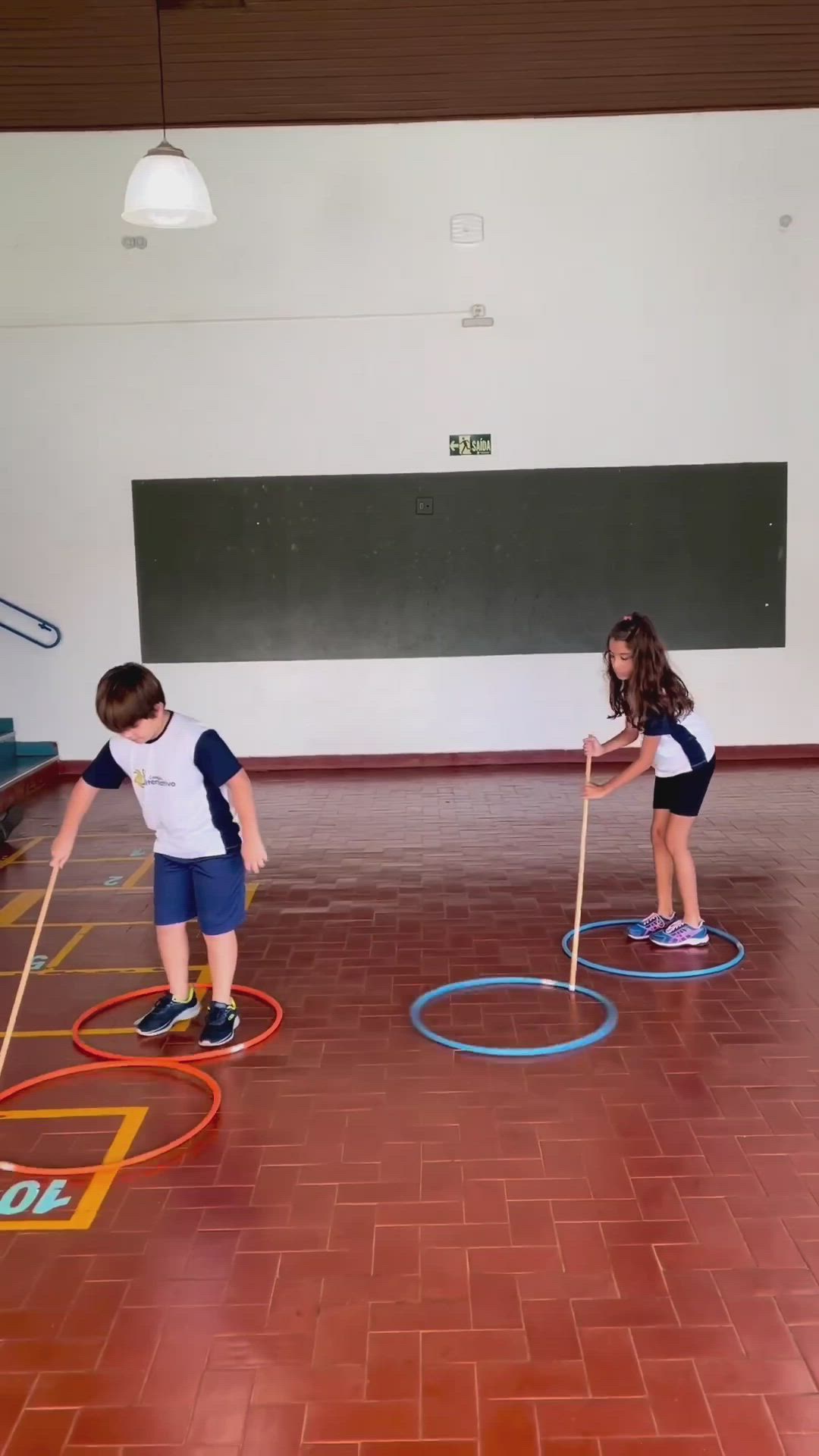 This may contain: two young children playing with colored circles in an indoor gym area, one boy is holding a stick and the other girl is standing behind him