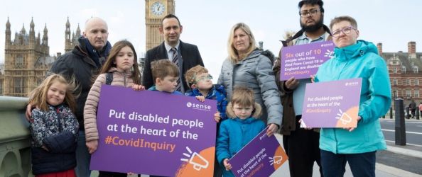 A group of children and adults hold purple placards on Westminster Bridge, with the Houses of Parliament in view behind them.