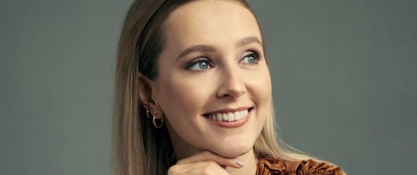 Rose Ayling-Ellis, a white woman with long blonde hair, smiles as she looks off-camera to the left.