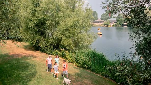 A family and their dog walk alongside a lake in the Cotswolds
