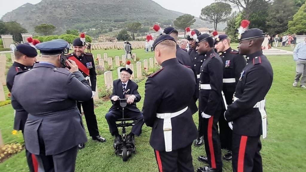 Men in uniform surrounding an elderly man in uniform on a mobility scooter