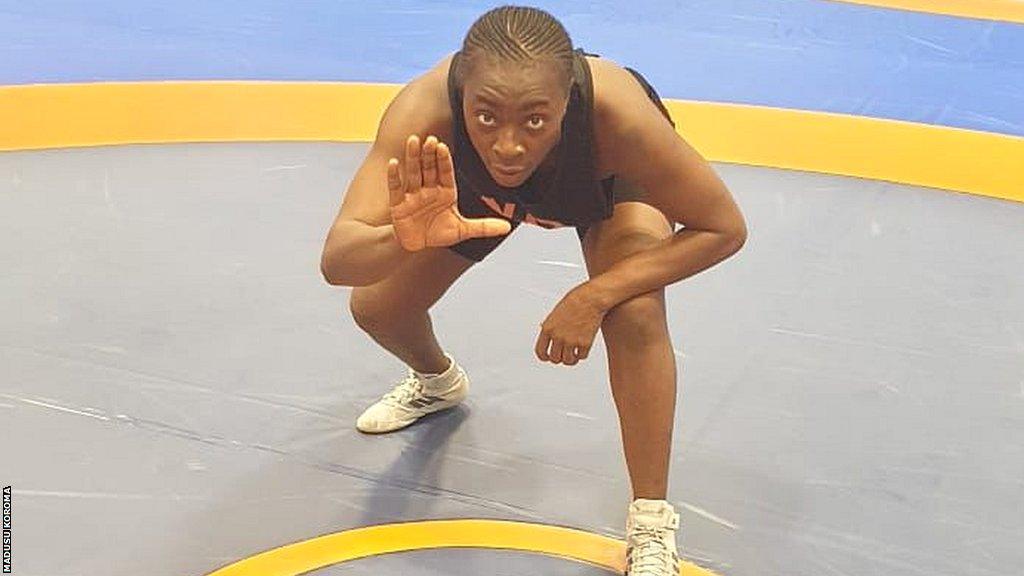 Madusu Koroma squats in wrestling pose in ring