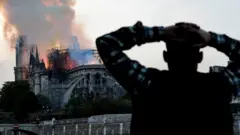 A man watches the landmark Notre-Dame Cathedral burn, engulfed in flames, in central Paris on April 15, 2019