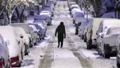 Улица и машины в снегу. По улице идет человек