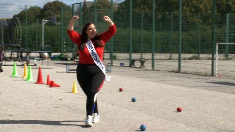 A woman with a red top and black sports leggings walks with her hands in the air on a sports field. 