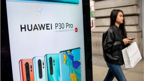 A woman walks past a bus stop ad for a Huawei smartphone in London
