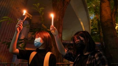 Two women hold candles near Victoria Park, June 2021