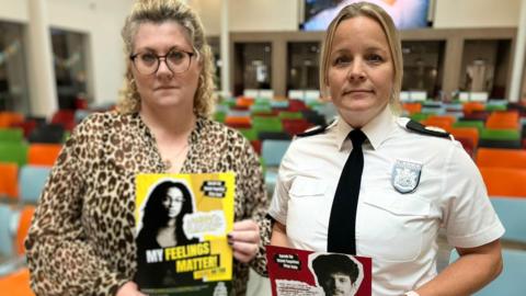 Lisa Squire and Assistant Chief Constable Katy Barrow-Grint look into the camera, holding a poster or leaflet saying 'my feelings matter'