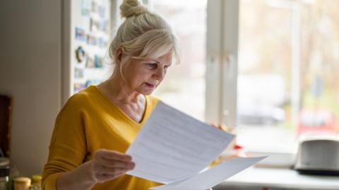 Woman locking at bills in kitchen (file image) 