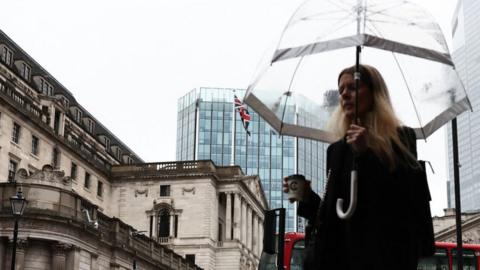 A pedestrian with an umbrella walks by the Bank of England building (L), in the financial district, central London, on November 2, 2023.