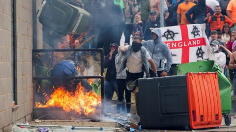 Protestors throw a garbage bin on fire outside a hotel housing asylum seekers in Rotherham, England on 4 August 2024 