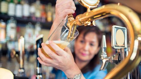 Bar tender pouring a pint of beer from a beer tap in foreground