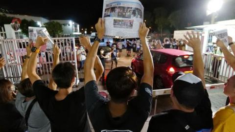 Apple Daily journalists hold freshly-printed copies of the newspaper's last edition while acknowledging supporters gathered outside their office in Hong Kong early on June 24, 2021,