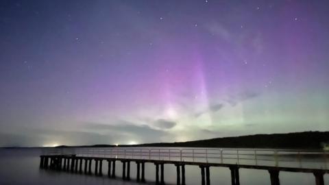 A walkway runs away from shore and the northern lights are displayed in the background 