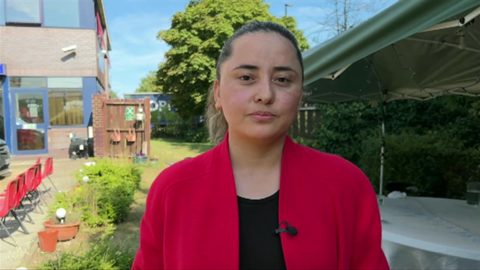 Sosan looks at camera. She is wearing a black top and red jacket, and has her hair tied back