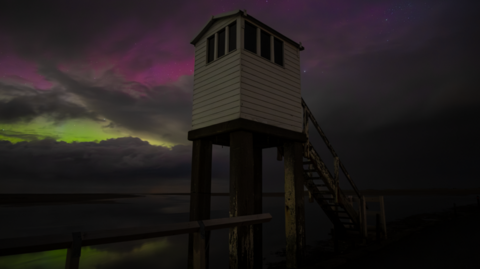 A refuge box with the northern lights visible through the clouds behind mostly yellow and pink 