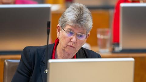 Jane Hutt, sat at her desk in the Welsh Parliament's debating chamber.