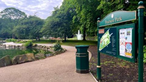 Pearson Park sign with a lake on the left and pathway surrounded by trees