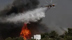 A firefighting helicopter tries to extinguish a wildfire threatening houses at the north-east suburb of Pallini, near Athens, Greece, 20 July 2022.