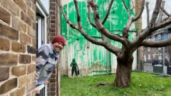 Carlos Serrano and the Bansky mural in Finsbury Park, London