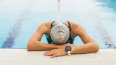 A woman in a swimming pool rests her head on the side of the pool