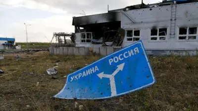 Дорожный знак со следами боев на фоне сгоревшего здания